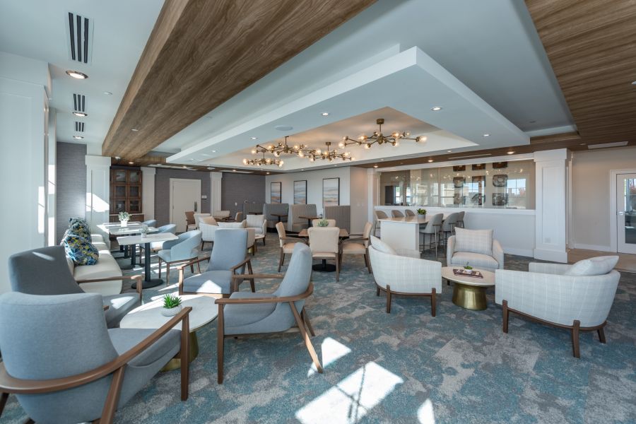 Modern lounge with gray and white armchairs, round tables, and large windows letting in natural light.