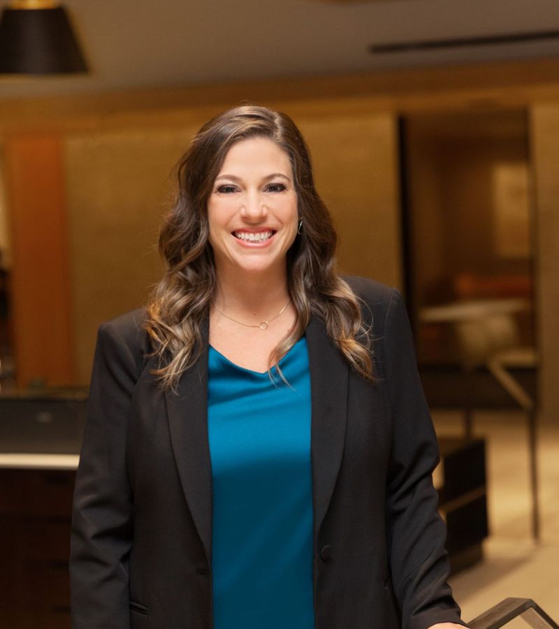 Woman in a black blazer and blue top smiling in an office setting.