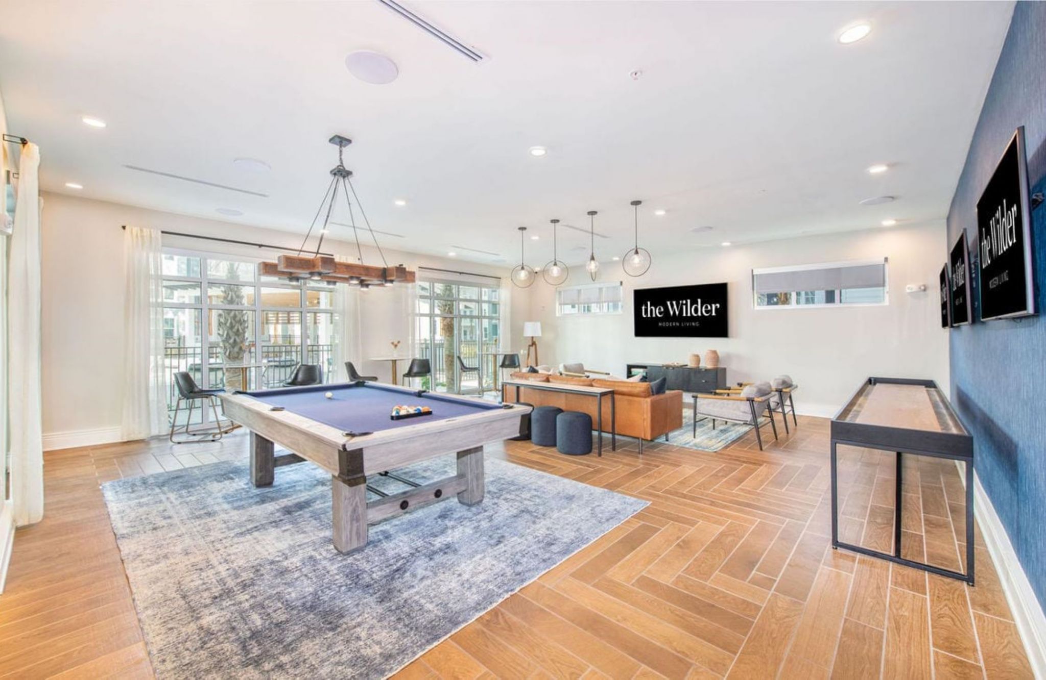 Modern recreation room with pool table, shuffleboard, and lounge area featuring a sign reading "the Wilder.