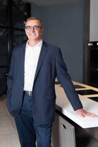 Smiling man in a suit stands next to a modern kitchen counter.